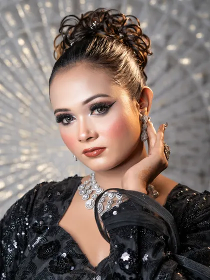 A high-fashion party look with a messy high bun and dramatic winged eyeliner. The skin is kept glowing and fresh.