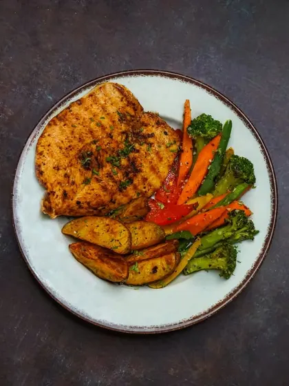 A hearty platter of grilled chicken breast served with roasted vegetables and potato wedges on a rustic plate.