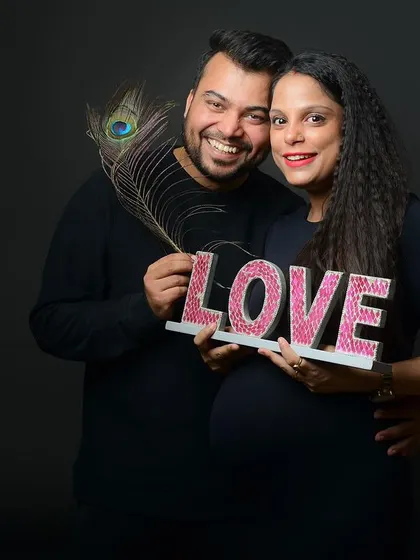 A fun and happy maternity portrait. Using props like the "LOVE" sign and a peacock feather adds a creative and personal element to the session.