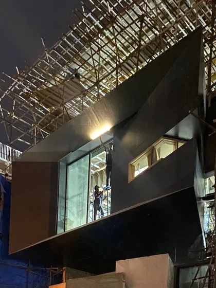The 'House of Reddys' at night during construction, with its angular, dark-clad facade beginning to take shape.