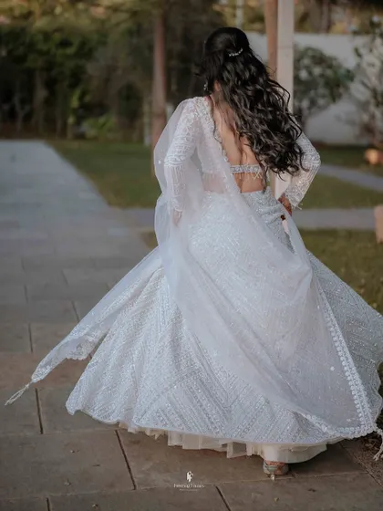 The back view of the bride in her white lehenga, showing the beautiful flow and detail of her outfit as she walks.