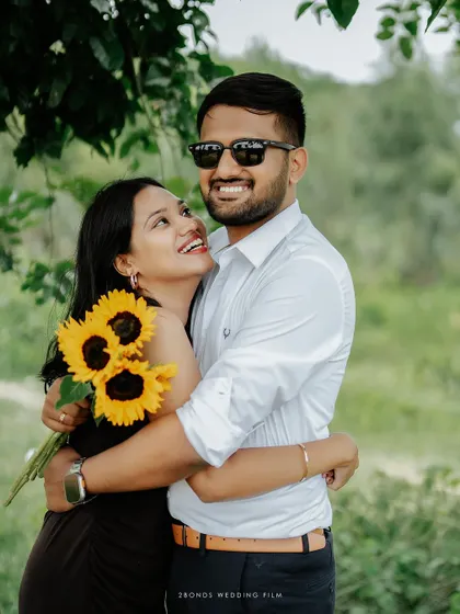 A bright, happy embrace under the shade of a tree, the bride's smile lighting up the frame as she looks at her partner.