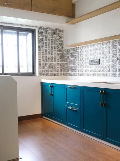 A wider view of the PU finish kitchen, showing the contrast between the dark teal base cabinets and the white upper cabinets. The open wooden shelf adds warmth and a space for decor against the patterned tile backsplash.
