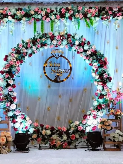 A beautiful floral ring stage for an engagement. The ring is adorned with pink and white flowers, set against a backdrop of white drapes and warm lights.