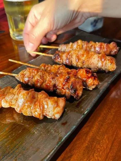 A hand reaching for a perfectly grilled Yakitori skewer. These are a classic izakaya (Japanese pub) snack, perfect for sharing.