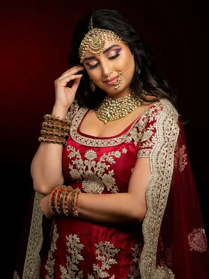A classic red lehenga look for a North Indian bride. The makeup is kept timeless with gold tones on the eyes and a warm red lip, complemented by a traditional maang tikka and nath.