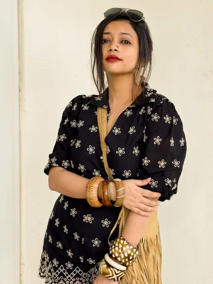 A close-up showing the embroidery on the romper and the stacked wooden bangles.