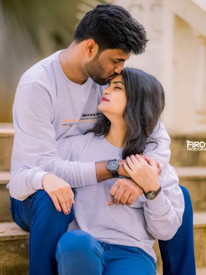 A tender forehead kiss, capturing a quiet, intimate moment. The couple's matching casual sweaters make this a very cozy and romantic pre-wedding photo.