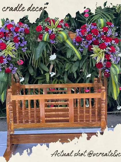 A baby cradle adorned with vibrant red and purple flowers, ready for a joyous naming ceremony.