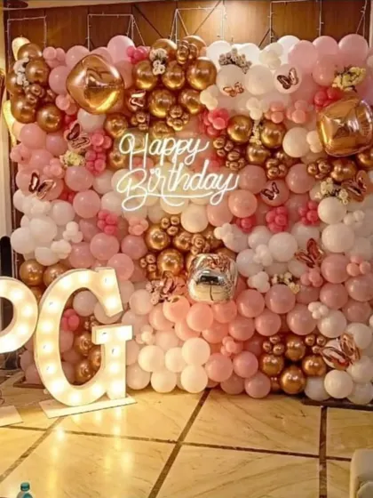 A dense and luxurious balloon wall in rose gold, pink, and white. This setup creates a massive photo-worthy backdrop, complete with a neon sign and large marquee letters for initials.