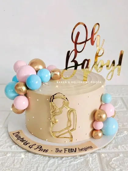 "Diapers & Pins, the fun begins." This baby shower cake uses a lovely beige base with pink, blue, and gold balloon clusters to celebrate the new arrival. The acrylic mom-to-be silhouette adds a personal touch.