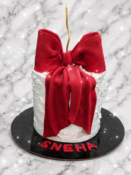 An elegant white cake that looks like a gift. The centerpiece is a large, beautifully crafted red fondant bow.