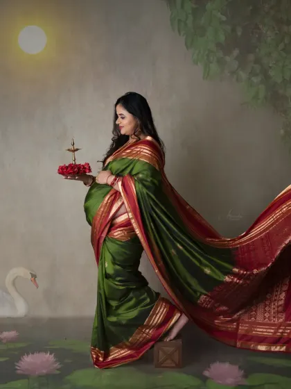 A stunning, artistic portrait of a mom-to-be in a green and red saree, holding a diya. The painted background with a full moon creates a magical atmosphere.