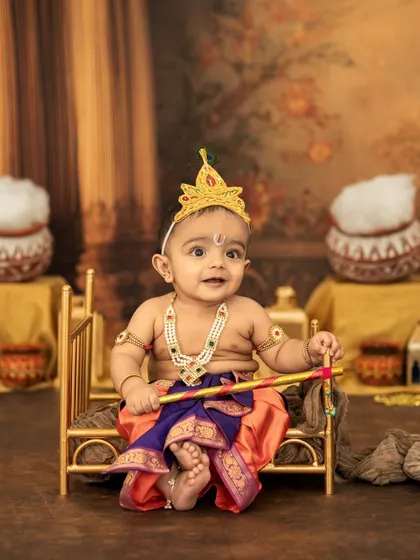 This little Krishna is ready for his close-up! His big, curious eyes and adorable costume make for an unforgettable portrait on his miniature golden bed.
