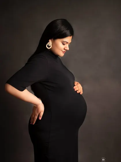 A classic three-quarter maternity portrait in black and white. The simple black dress and dark background create a timeless and sophisticated feel.