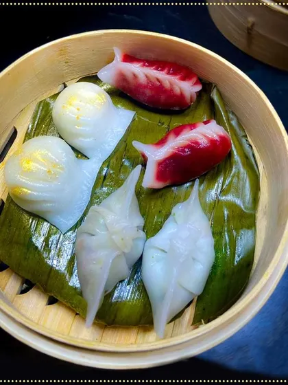 An assortment of delicate dim sum, including colorful and intricately shaped dumplings. Served on a banana leaf in a bamboo steamer, this dish is a feast for the eyes and the palate.