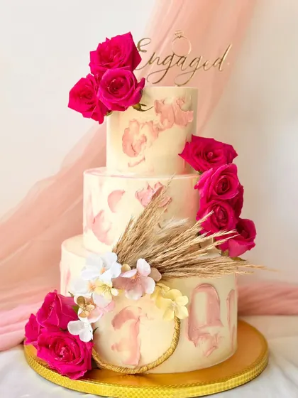 This three-tier engagement cake is a showstopper, featuring a textured pink buttercream effect and adorned with vibrant fresh magenta roses and dried wheat.