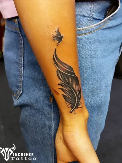 A delicate feather that transforms into a flying bird was used to cover up a small name tattoo on this client's forearm. This design symbolizes freedom and moving on.