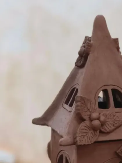 A close-up view of a terracotta house lantern, showing the delicate, hand-sculpted leaves and berries adorning the roof. Every detail is crafted with patience and care.