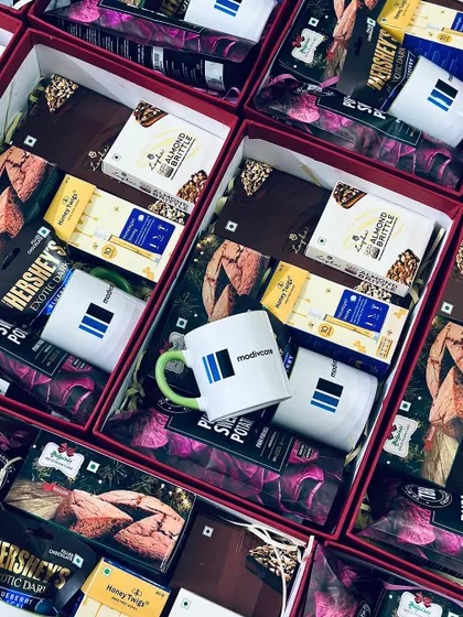 An overhead view of multiple corporate gift boxes for Modiwave, each containing a branded mug and a selection of premium chocolates and snacks.