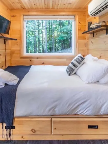 This cozy bedroom in a wooden container home is perfect for a nature retreat. The window provides a beautiful view of the forest, and the built-in storage under the bed is a practical space-saving solution.