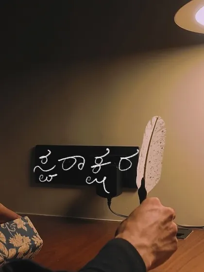 Another shot from the 'Svarakshara' video, showing the song title written in Kannada on a modern desk setup. This blends traditional script with a contemporary aesthetic.