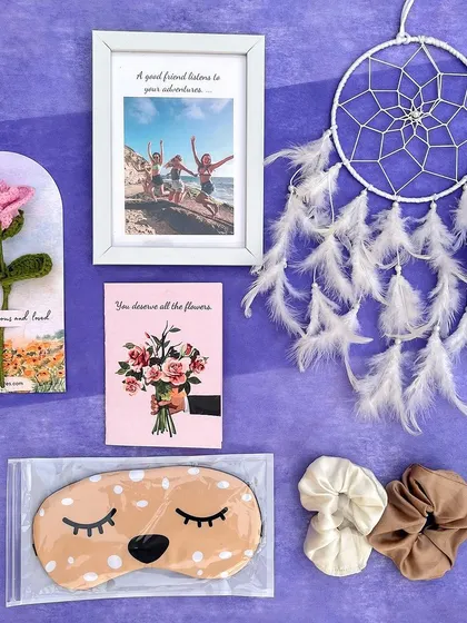 A closer look at the items in our pamper hamper. It includes a crochet rose on a card, a custom photo frame, a dream catcher, a relaxing eye mask, and soft scrunchies.