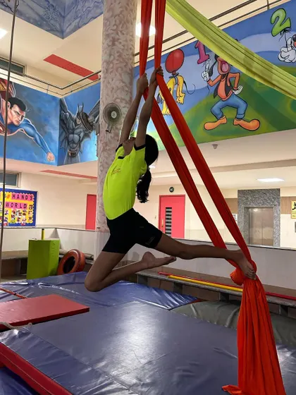 A young student reaches high, practicing a climbing pose that builds upper body strength and technique.