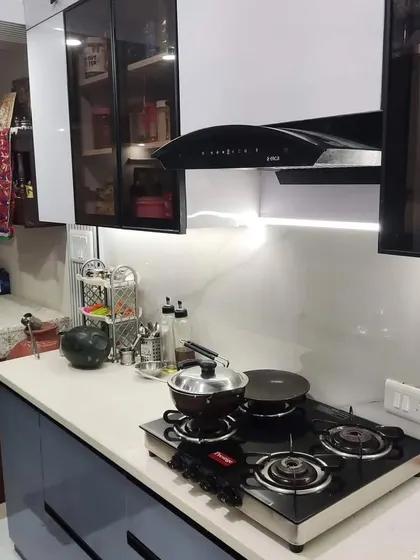 A close-up of our completed kitchen at Paras Tieria, Noida. This view highlights the Inotech gloss finish on the cabinets, the sleek black chimney, and the under-cabinet profile lighting.
