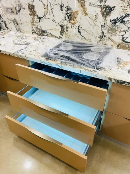 Our drawers are as beautiful inside as they are outside. This image shows a set of handleless drawers with a high-gloss finish, revealing the organized cutlery tray and smooth inner mechanism.