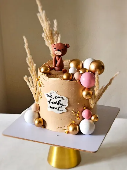 A boho-themed baby shower cake, perfect for a modern celebration. This design uses dried pampas grass, earthy tones, and a cute teddy bear topper.