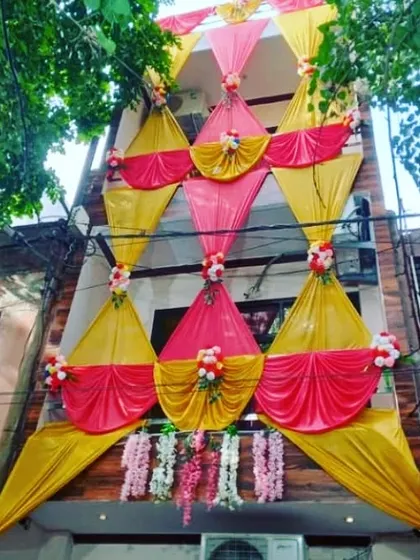 An elaborate house facade decoration with a multi-layered design of pink and yellow drapes and floral accents.