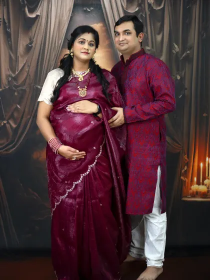 A traditional and glamorous maternity session. The couple is dressed in elegant ethnic wear, creating a rich and culturally beautiful portrait against a classic painted backdrop.