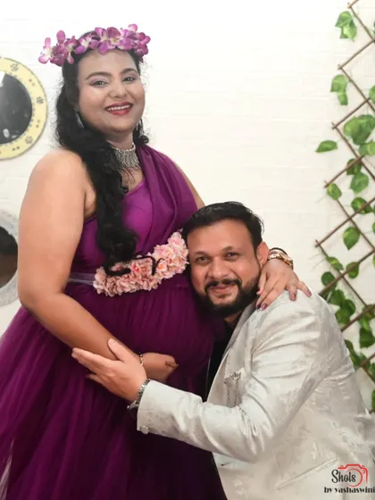 A sweet moment between expecting parents. She is wearing our one-shoulder purple gown, and he is in a stylish white blazer, also available for rent.