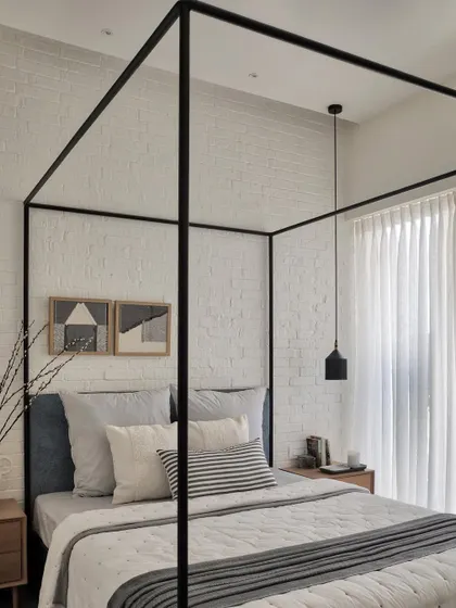 The daughter's love for white inspired this bedroom design. The four-poster bed is accentuated by a rustic white brick wall, while oak side tables add a touch of warmth and coziness, creating a dreamy and timeless space.