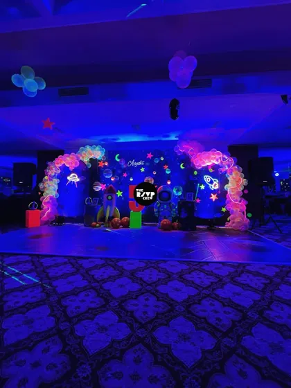 The dance floor is ready for blast-off. This wide shot shows the full neon space setup, complete with a galaxy-themed floor mat and glowing balloon arches.