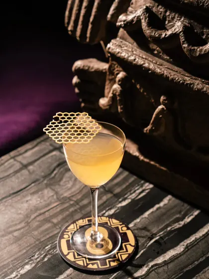 A close-up of a craft cocktail at Ocho Bandra, featuring a unique honeycomb-patterned garnish. The moody lighting and marble tabletop add to the sophisticated feel.