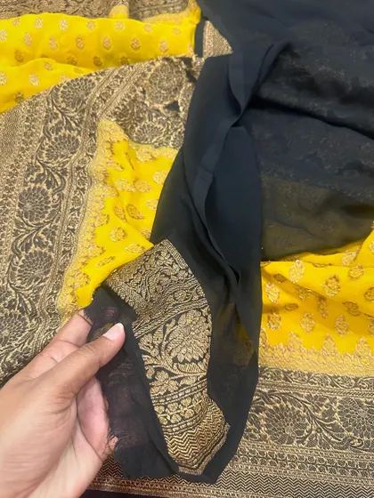 The plain black blouse piece for the yellow Kadi georgette saree, with its intricately woven floral border.