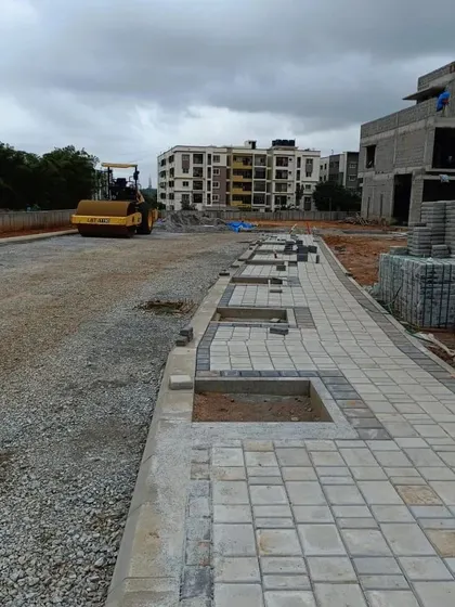 A work-in-progress view of a residential street under construction. This shot captures the different stages of site development, from the compacted road base in the background to the nearly completed pedestrian walkway with allocated spaces for tree planting.