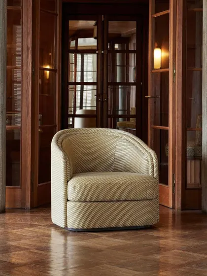 The "Boromeo" armchair, a timeless and enveloping design defined by its elegant double-curved backrest. Upholstered in a subtle geometric fabric, it stands as a singular piece of sophisticated comfort.