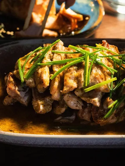 A plate of Chicken Anticucho, with the light catching the glistening sauce and fresh chives. The shot is warm and inviting.