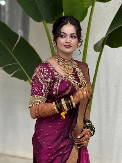A three quarter view of the bride's final look. The wine-colored silk saree is draped to showcase its golden border and the rich texture of the fabric.
