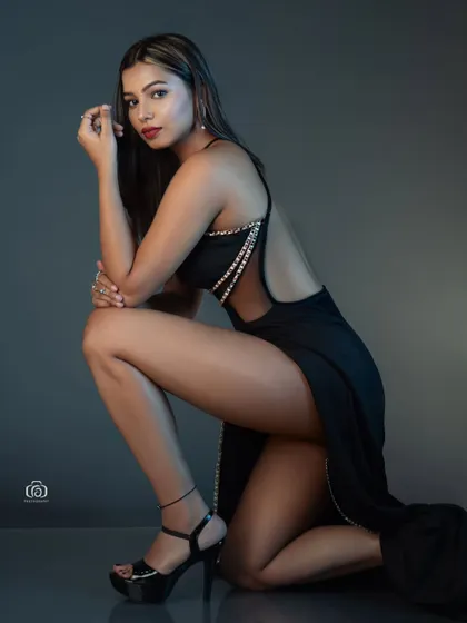 A low-angle shot that emphasizes the drama of a high-slit black gown. The lighting is focused to create a sense of intimacy and highlight the elegant lines of the dress.