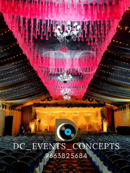 A full view of an indoor venue transformation. The ceiling is adorned with dramatic pink and black drapery and chandeliers, while the seating is perfectly arranged to face the main stage.