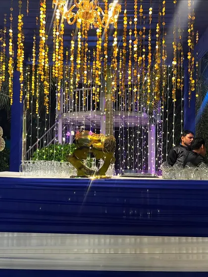 A glimpse of a royal blue and gold themed bar setup. The decor features hanging golden sequin strings and a chandelier, creating a sparkling and luxurious corner for guests to enjoy their drinks.