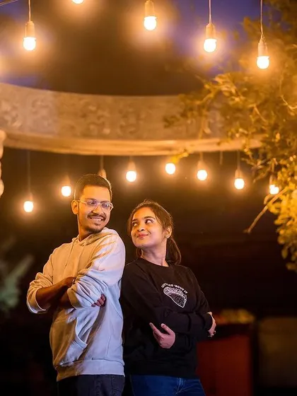 A playful and stylish night shot of a couple under hanging Edison bulbs.