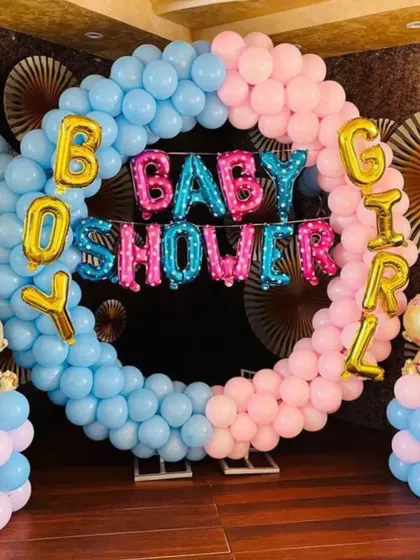 A "Boy or Girl" baby shower photo booth. The circular frame is made of pink and blue balloons, with foil letters and baby-themed foil balloons on the sides.
