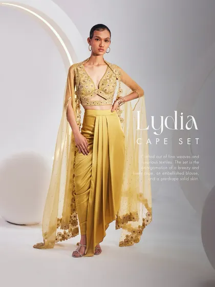 The Lydia Cape Set in gold, featuring a breezy and lively cape, an embellished blouse, and a pre-draped solid dhoti skirt. A favorite for its fusion appeal.