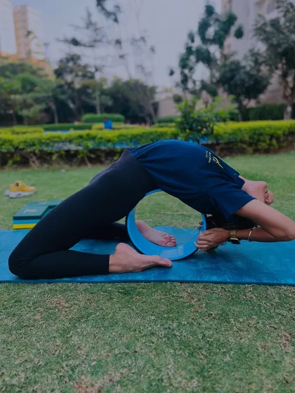 A student using a yoga wheel to deepen her backbend in the park. Practicing outdoors adds another layer of connection to the experience.