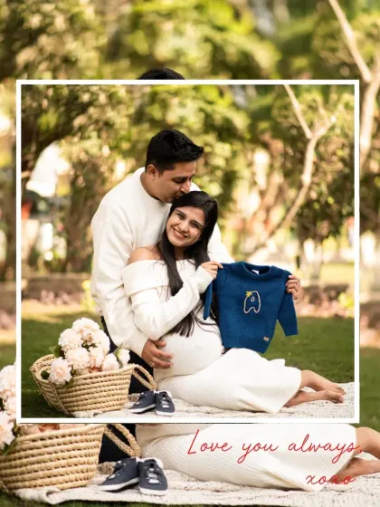 A cozy and sweet outdoor picnic scene. The couple shares a tender moment, surrounded by flowers and props like a tiny sweater, making for a lovely announcement photo.